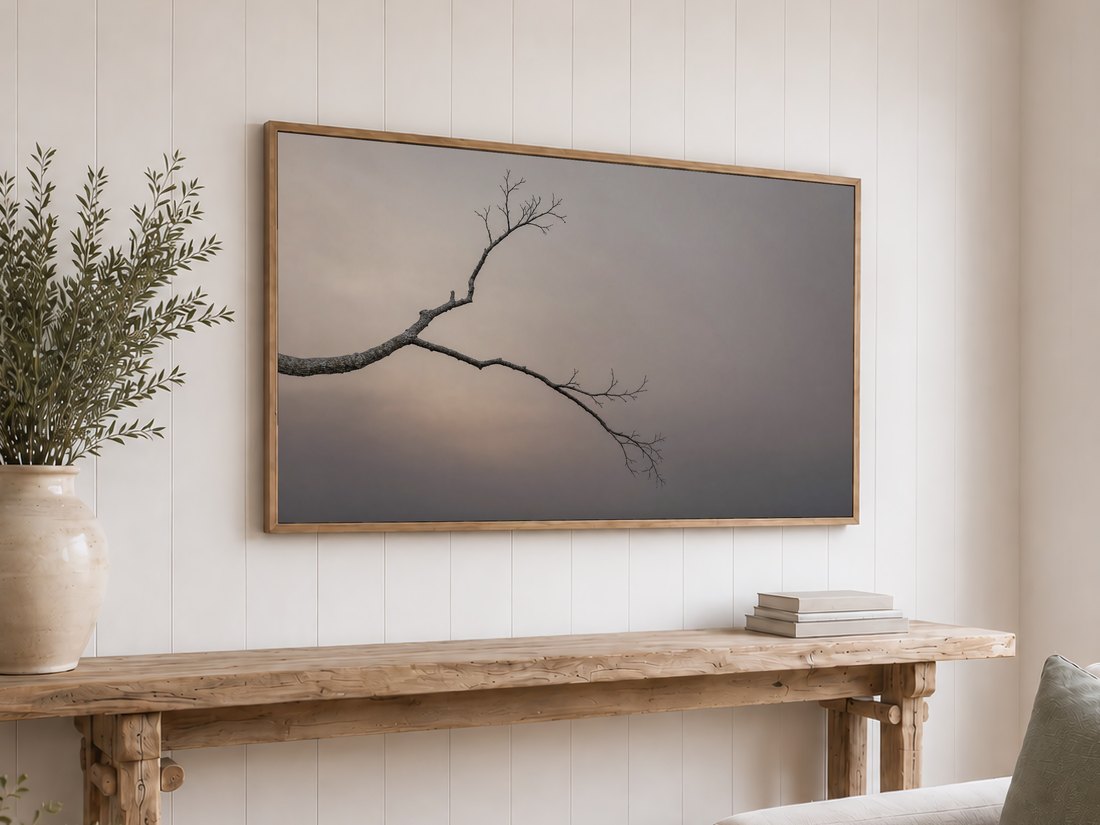 Bare branch photo shown on a light oak framed TV above a rustic reclaimed-wood console table with olive branches in a cream vase and neutral books, set against a white shiplap wall.