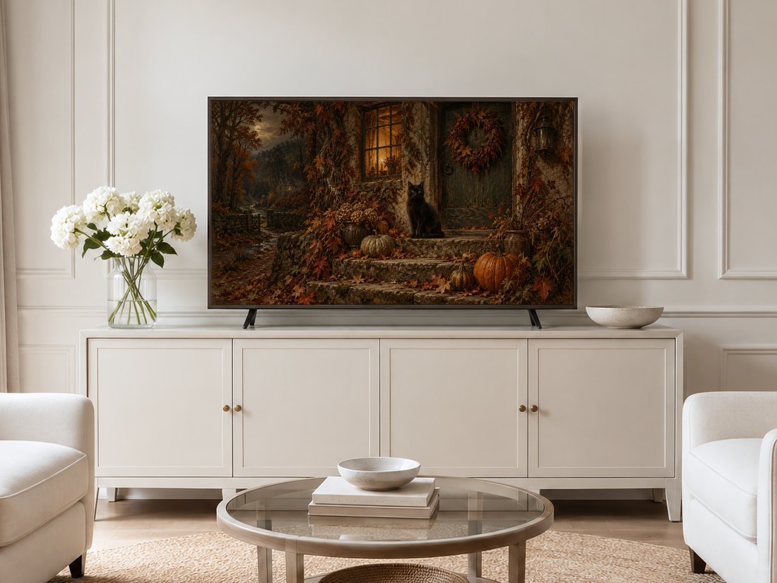 Black cat at cottage door autumn landscape displayed on Frame TV in neutral living room with cream sideboard, white hydrangea arrangement and pale upholstered chairs.