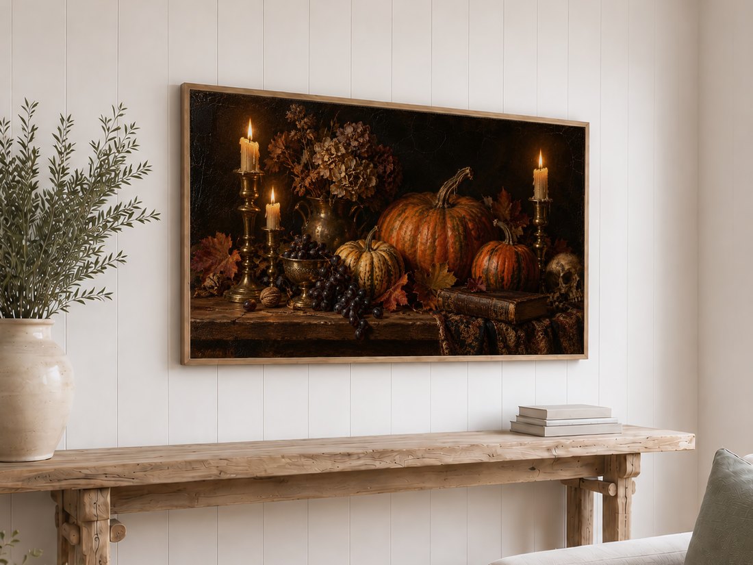 Glowing pumpkin and candle still life shown on a Frame TV above a rustic reclaimed-wood console on white shiplap, with cream ceramic vase holding olive branches and stacked neutral books.