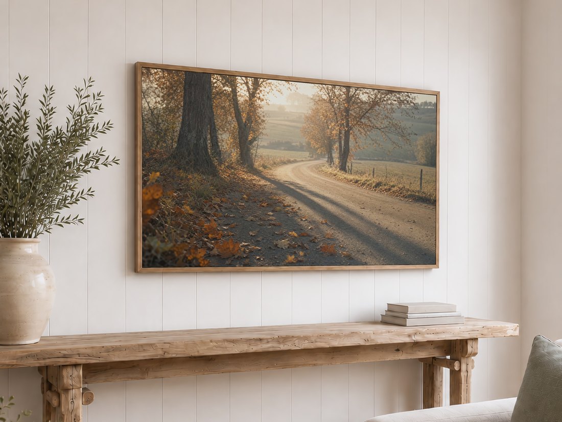 Painterly autumn road artwork on a light oak framed TV above a reclaimed-wood console with olive branches and neutral books, set against a white shiplap wall for cozy fall decor.