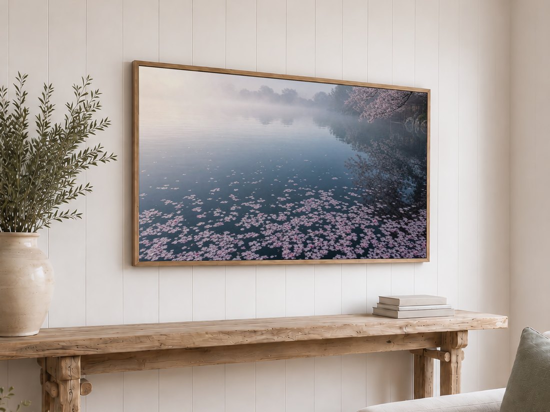 Cherry blossom pond art displayed on a light oak framed TV against a white shiplap wall, above a reclaimed-wood console with olive branches and neutral books, for a calm coastal-farmhouse feel.