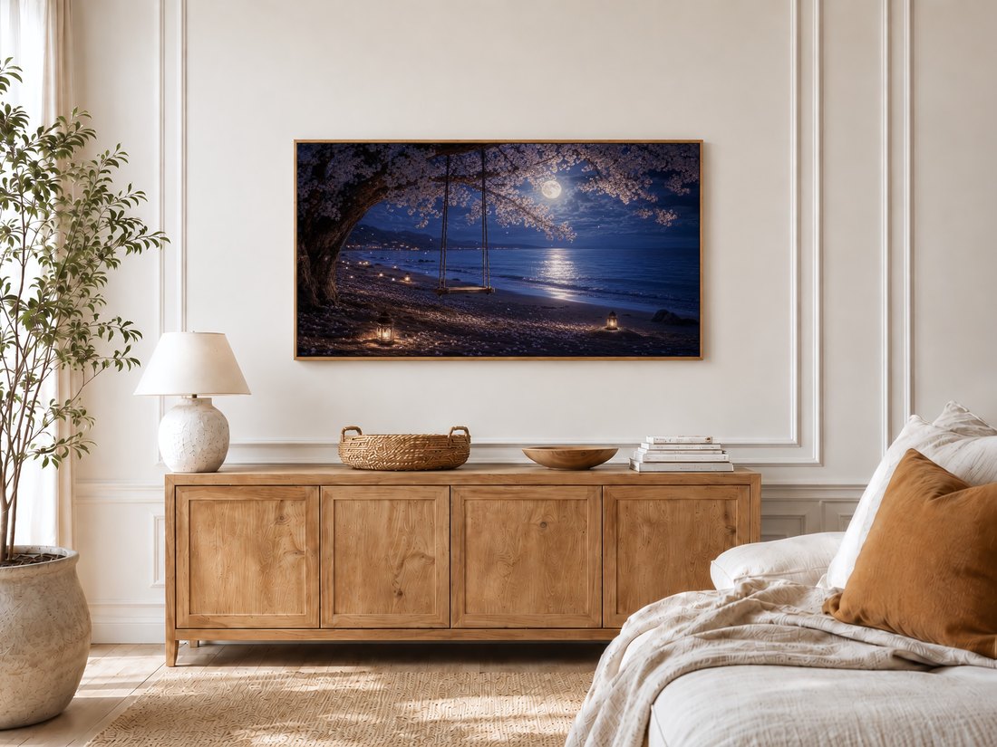 Moonlit sakura beach swing art on a Frame TV in a bright bedroom with cream panelled moulding, a light oak sideboard, ceramic lamp, rattan tray, potted olive tree and a linen bed dressed with a rust cushion.