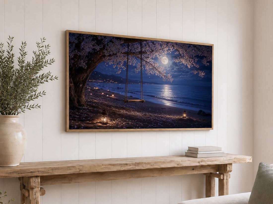 Dreamy cherry blossom night beach artwork on a light oak framed TV against a white shiplap wall, above a rustic reclaimed-wood console table styled with olive branches in a cream vase and a stack of neutral books.