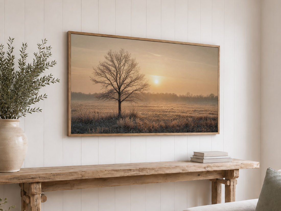 Lone frosted tree at hazy sunrise on a light oak framed TV above a reclaimed-wood console with olive branches and neutral books, set against a white shiplap wall.