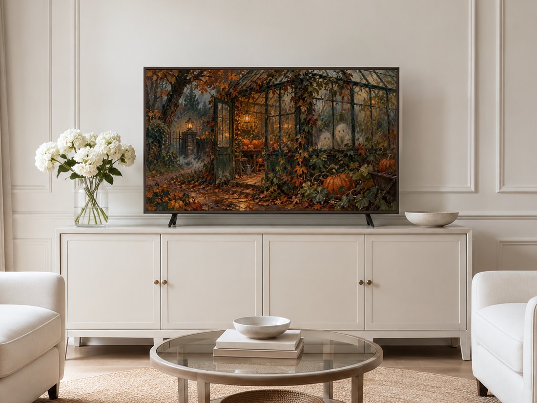 Autumn Pumpkin Greenhouse Frame TV Art shown on a Frame TV in a neutral living room with cream panelled walls, cream sideboard topped with white hydrangeas in a glass vase, round glass coffee table and pale armchairs on a jute rug.