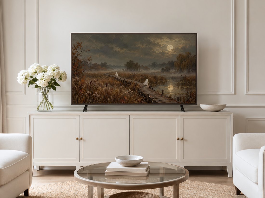 Moody autumn landscape with ghostly figures on a moonlit boardwalk shown on a Frame TV mounted on a neutral cream panelled wall above a cream sideboard with brass knobs and white hydrangeas
