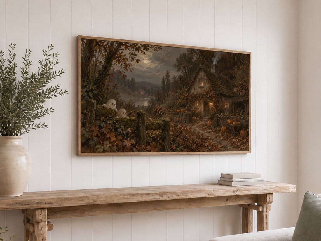 Haunted Autumn Cottage Frame TV Art in a light oak frame on white shiplap above a reclaimed-wood console table with cream ceramic vase of olive branches and neutral books.