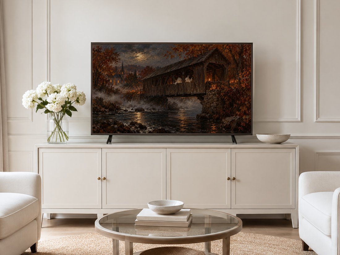 Moody Halloween scene with a ghostly bridge over dark water beneath a full moon and golden trees, displayed on a Frame TV in a neutral living room with cream panelling, white hydrangeas and a round glass coffee table.