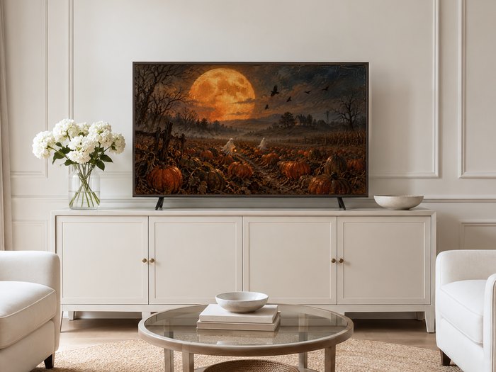 Harvest Moon Over the Pumpkin Field displayed on Frame TV in a neutral cream living room with sideboard, white flowers, glass coffee table and pale armchairs on jute rug.