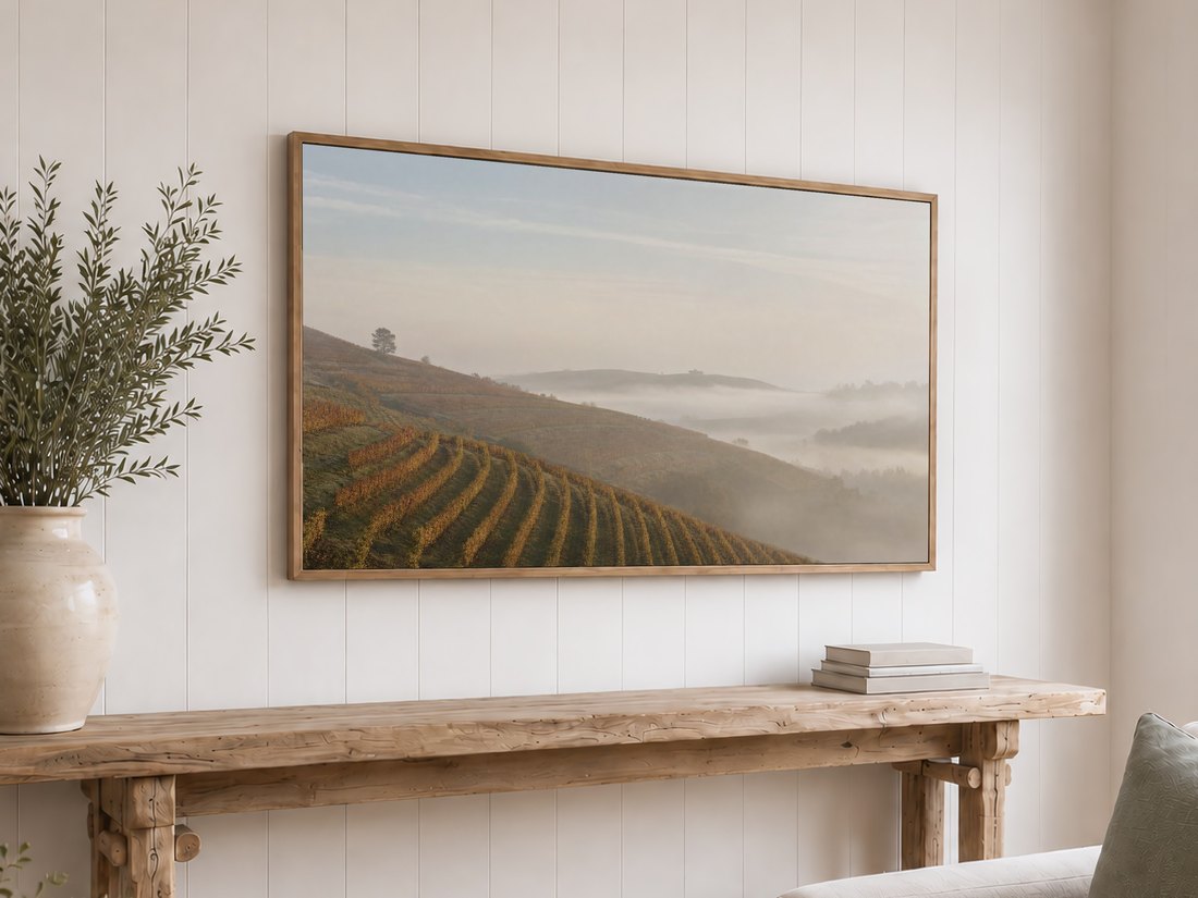 Foggy vineyard terrace art on an oak framed TV above a reclaimed-wood console with olive branches, the muted gold hillside and rolling mist bringing a rustic, sunlit calm to this shiplap wall setting.