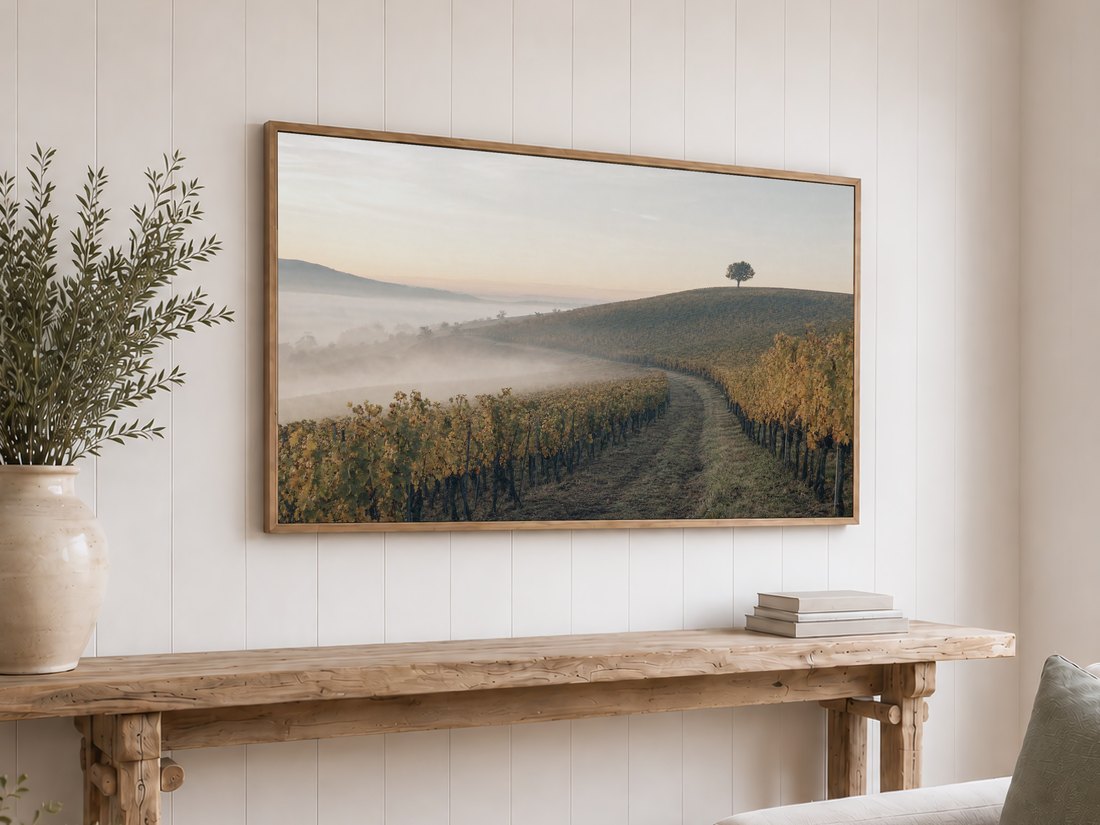 Autumn vineyard row art with fog and a distant tree displayed on a light oak framed TV above a reclaimed-wood console with olive branches, suited to a rustic neutral room.