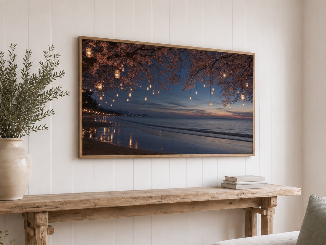 Cherry blossom lantern beach scene at dusk shown on a light oak framed Frame TV against a white shiplap wall, above a reclaimed-wood console table with olive branches in a cream ceramic vase and a stack of neutral books.