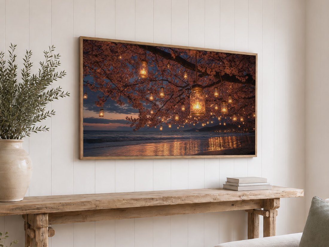 Cherry blossom lantern beach art on a light oak framed TV mounted on a white shiplap wall, above a rustic console table with olive branches in a cream ceramic vase and a stack of neutral books.