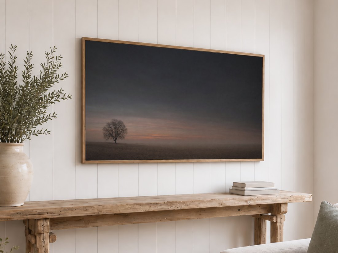 Lone bare tree in a foggy field shown on a light oak framed TV against a white shiplap wall, with olive branches and neutral books on the console table below, bringing calm to a farmhouse style space.