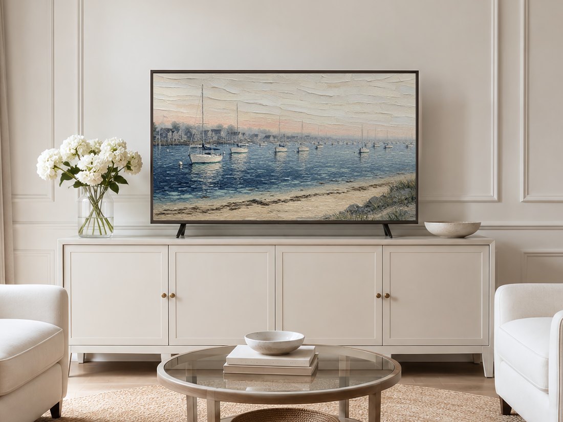 Coastal sailboat harbor artwork displayed on a Frame TV in a neutral living room with a cream sideboard, white hydrangeas, and pale armchairs, adding a calm nautical touch to the space.