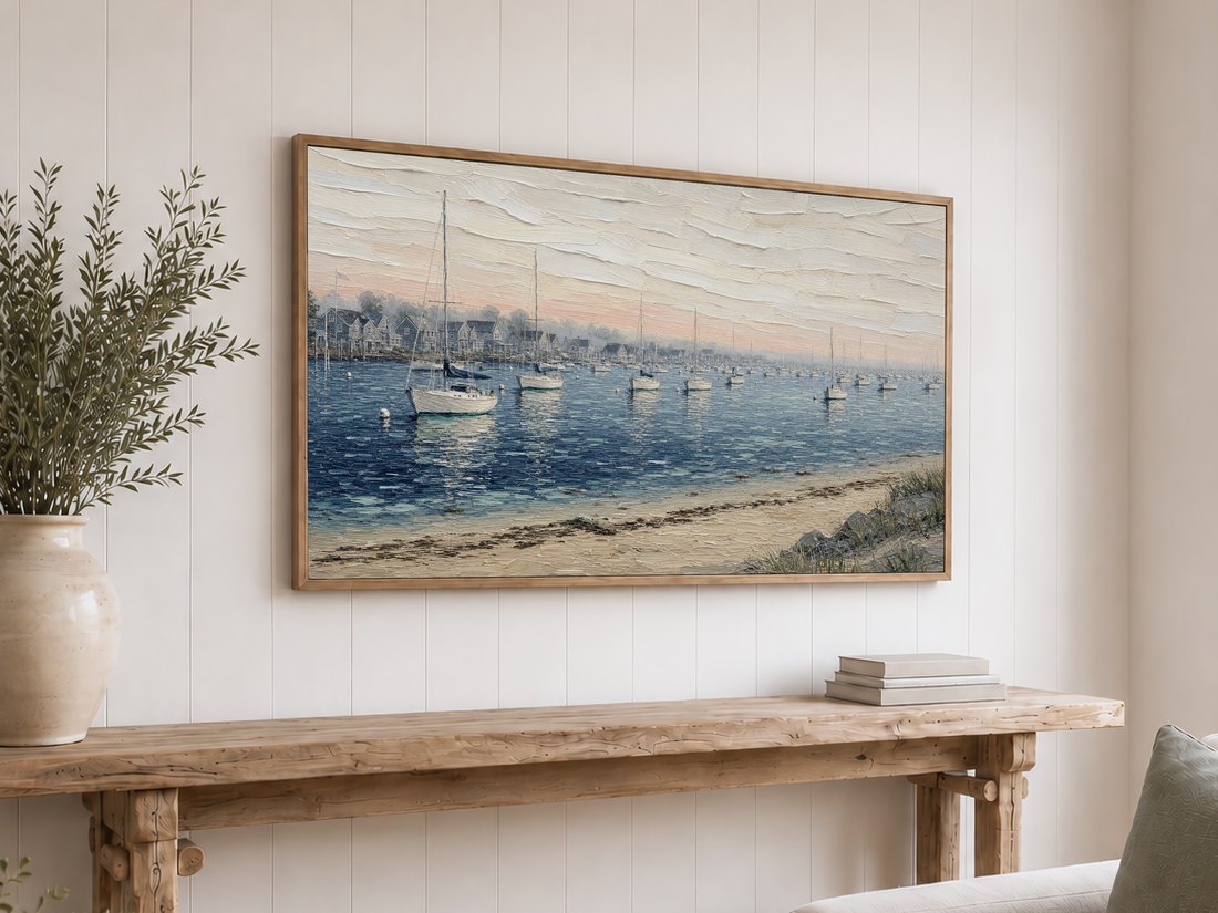New England harbor scene with moored sailboats shown on a Frame TV above a rustic reclaimed-wood console table with olive branches, set against a white shiplap wall for a coastal cottage look.