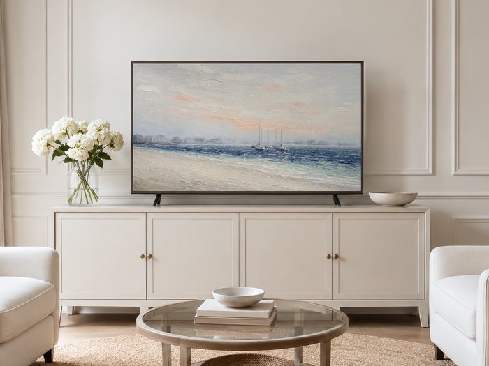 Misty harbor seascape with sailboats shown on a Frame TV in a neutral living room with a cream sideboard, white hydrangeas and pale armchairs on a jute rug, adding coastal calm to the space.