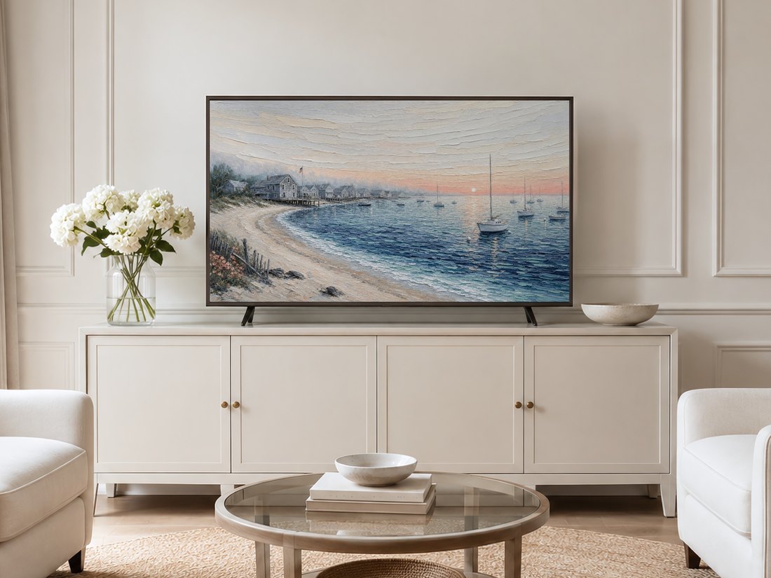 Coastal harbor sunrise Frame TV art in a neutral living room with a cream panelled wall, cream sideboard, white hydrangeas, glass coffee table and pale armchairs on a jute rug.