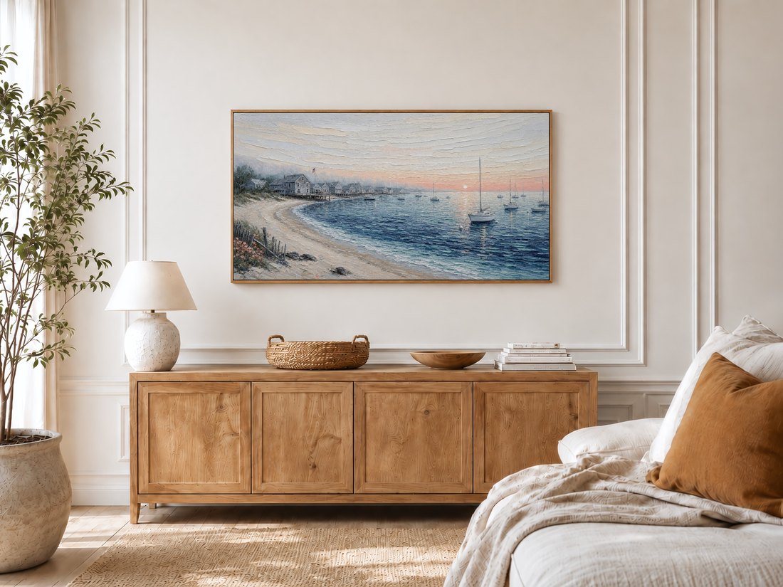 Sailboat harbor artwork shown in a bright bedroom with cream panelled moulding, an oak sideboard, ceramic lamp, potted olive tree and a linen bed with a rust cushion.