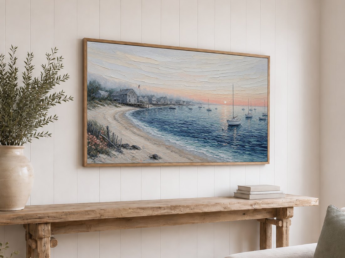 Coastal cottage seascape framed in light oak above a reclaimed-wood console with olive branches in a ceramic vase and neutral books, set against a white shiplap wall.