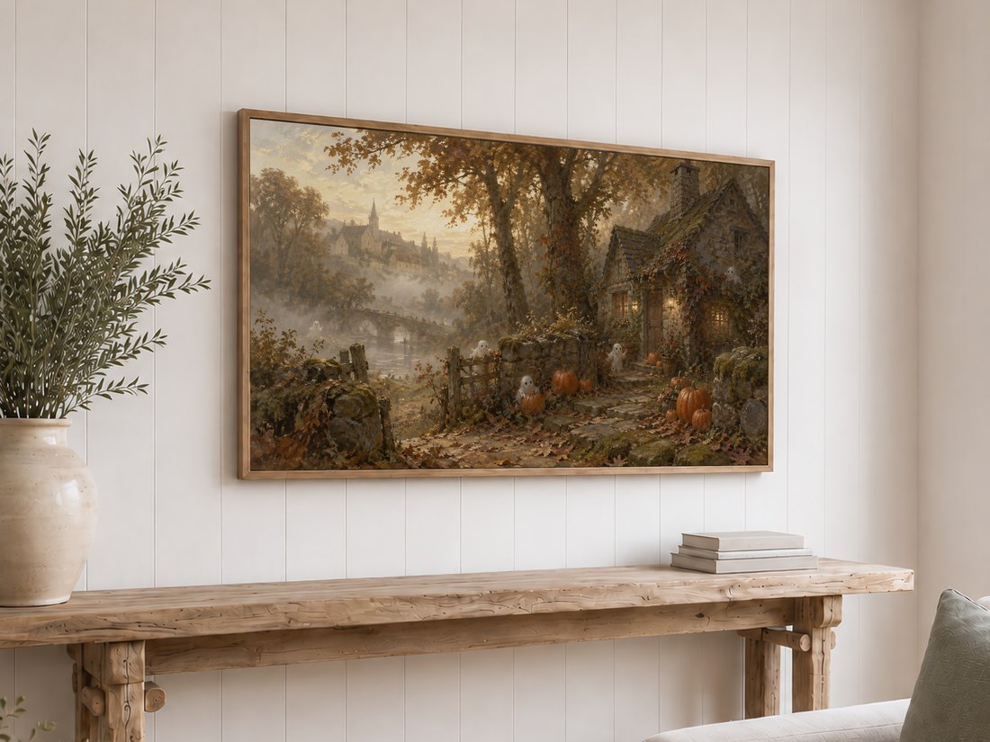Enchanted autumn village with stone bridge and glowing cottage displayed on a Frame TV above a reclaimed-wood console table with olive branches in cream ceramic vase and neutral books.