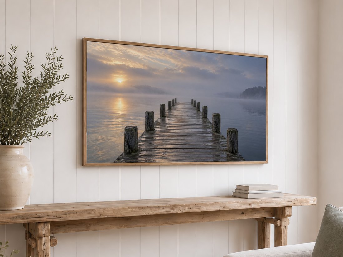 Tranquil misty pier scene on Frame TV in light oak frame above reclaimed-wood console with olive branches in cream vase, set against white shiplap wall in bright bedroom