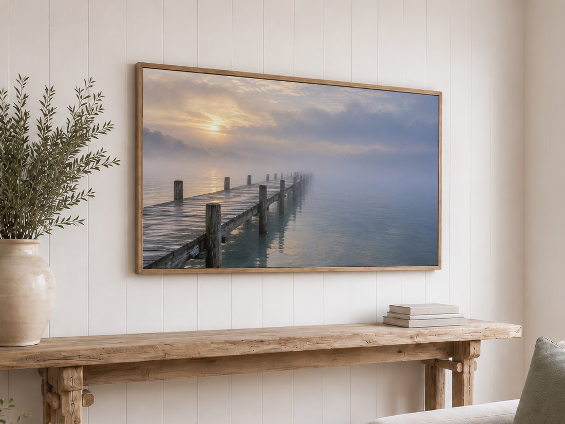 Misty pier landscape on frame TV above white shiplap wall with reclaimed-wood console table, olive branches in cream ceramic vase and stack of neutral books below