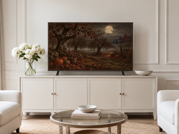 Moonlit Apple Orchard artwork shown on a Frame TV mounted on a neutral cream panelled wall above a cream sideboard with brass knobs, flanked by pale armchairs and white hydrangeas in a glass vase.
