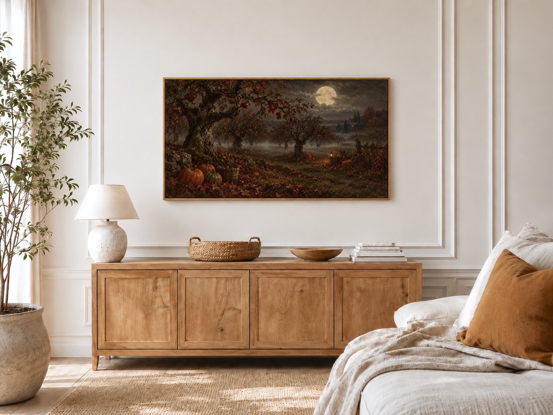Moonlit Apple Orchard art shown on a Frame TV in a bright bedroom with cream panelled moulding, light oak sideboard, textured ceramic lamp and a potted olive tree by the window.