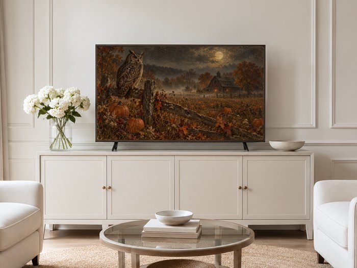 Moonlit owl and pumpkin field artwork displayed on a neutral living room Frame TV above a cream sideboard, with white hydrangeas and pale armchairs on a jute rug.