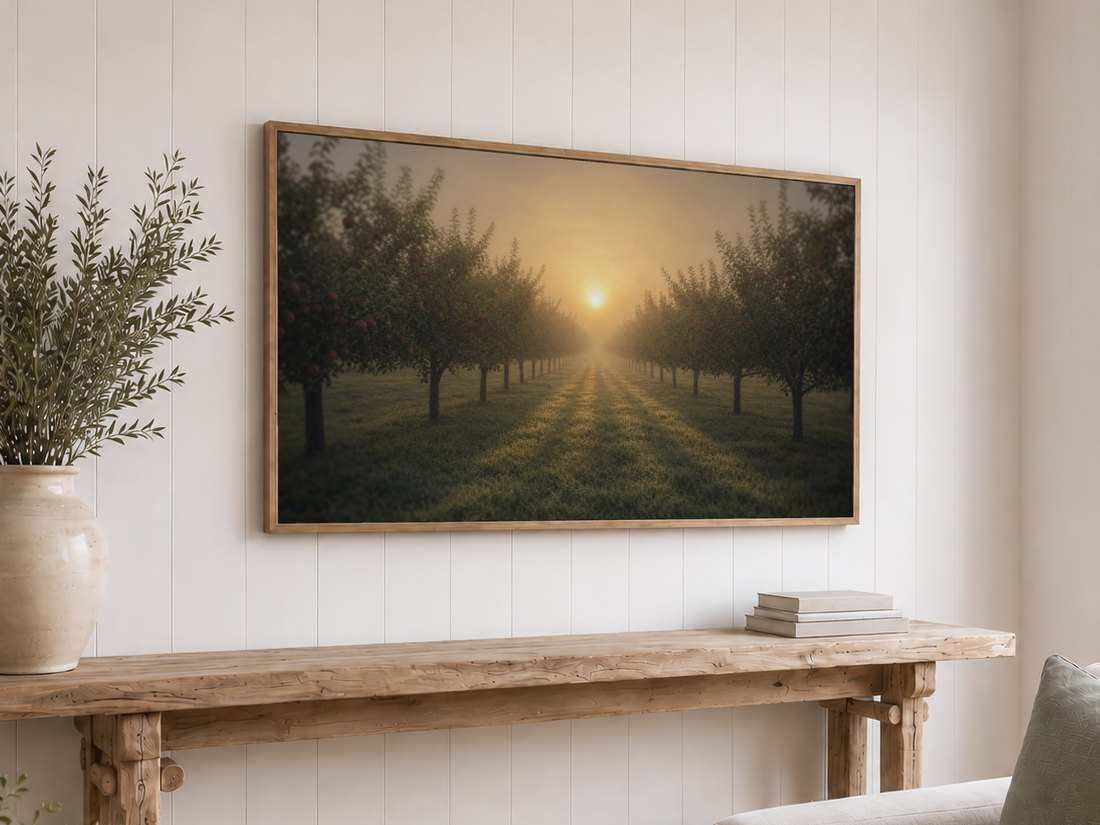 Amber sunrise orchard artwork on a light oak framed TV above a rustic reclaimed-wood console with olive branches in a ceramic vase and neutral books, set against a white shiplap wall.