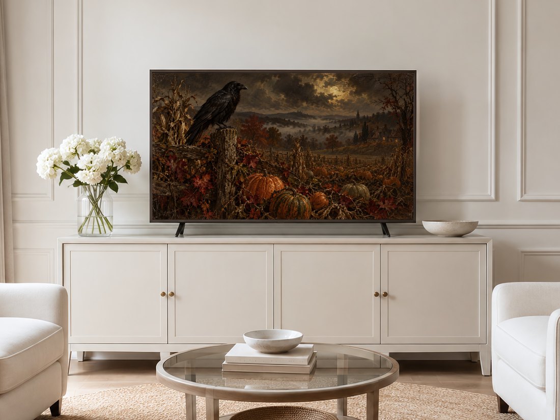 Frame TV art of raven and autumn pumpkin patch with golden atmospheric lighting shown on cream panelled wall in neutral living room with cream sideboard, white hydrangeas and pale armchairs.
