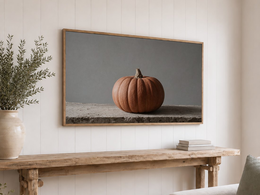 Muted terracotta pumpkin art on an oak-framed TV above a reclaimed-wood console with olive branches and neutral books, set against a white shiplap wall for autumn wall decor.