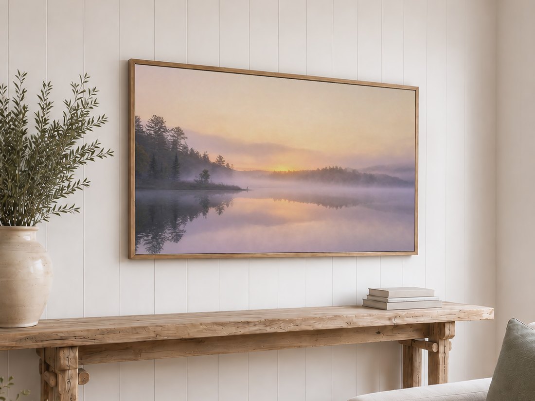 Foggy sunrise lake scene shown on a light oak framed TV above a reclaimed-wood console with olive branches and neutral books, the hazy heron landscape bringing quiet nature into a shiplap-walled room.