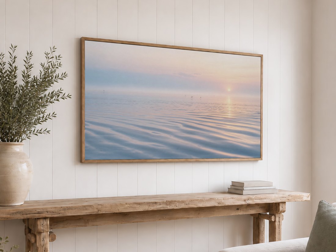Hazy tidal flat artwork on a light oak framed TV against a white shiplap wall, paired with a rustic console table, olive branches and neutral books, offering a calm coastal focal point for the room.