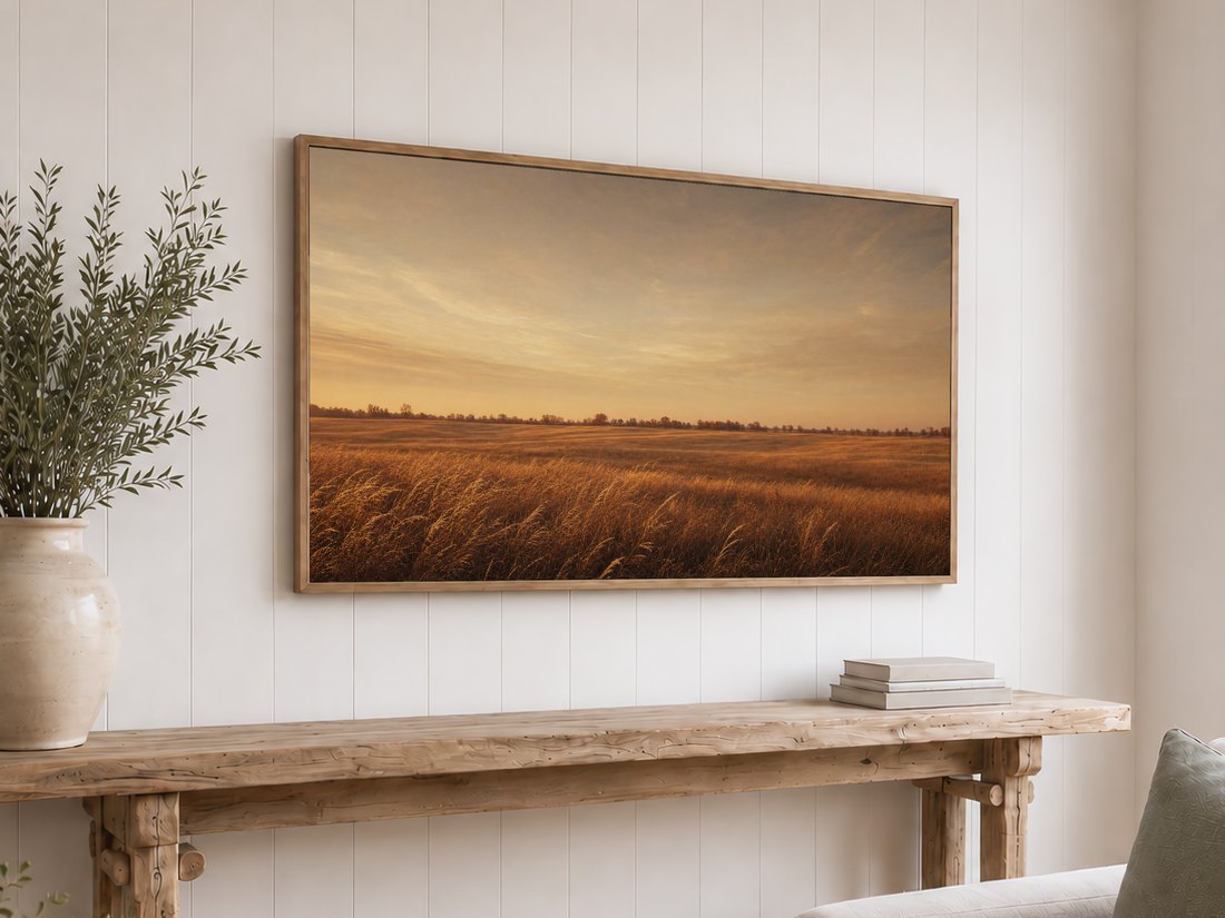 Rustic prairie sunset art on a light oak framed TV against a white shiplap wall, above a reclaimed-wood console with olive branches in a cream vase and a stack of neutral books, for a warm cottage feel.