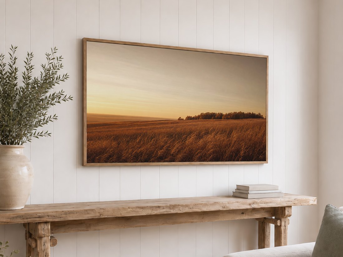 Golden prairie field art on a light oak framed Frame TV against a white shiplap wall, above a reclaimed-wood console with olive branches in a cream vase and neutral books, for a rustic calming display.